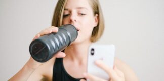 Woman drinking water while using a smartphone in a home fitness setting, highlighting modern technology and hydration.