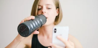 Woman drinking water while using a smartphone in a home fitness setting, highlighting modern technology and hydration.