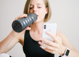Woman drinking water while using a smartphone in a home fitness setting, highlighting modern technology and hydration.