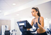 Serious fit woman in earphones and activewear listening to music and running on treadmill in light contemporary sports center