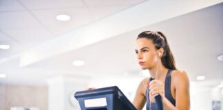 Serious fit woman in earphones and activewear listening to music and running on treadmill in light contemporary sports center