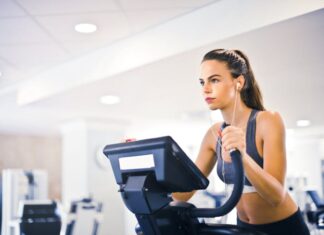 Serious fit woman in earphones and activewear listening to music and running on treadmill in light contemporary sports center