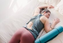 A woman in activewear resting on a bed with a yoga mat, symbolizing relaxation and fitness.