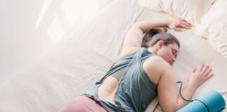 A woman in activewear resting on a bed with a yoga mat, symbolizing relaxation and fitness.