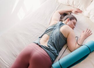 A woman in activewear resting on a bed with a yoga mat, symbolizing relaxation and fitness.