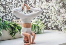 A woman performs a yoga headstand pose indoors surrounded by white flowers, symbolizing balance and fitness.
