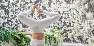 A woman performs a yoga headstand pose indoors surrounded by white flowers, symbolizing balance and fitness.