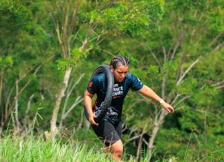 Como aumentar a resistência física com corrida em 5 passos A woman carries a tire outdoors during a fitness challenge surrounded by greenery.