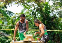 Two adults engage in a challenging outdoor team-building exercise with wooden obstacles.
