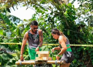 Two adults engage in a challenging outdoor team-building exercise with wooden obstacles.
