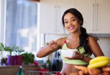 Smiling young woman in sportswear enjoying a healthy fruit snack indoors.