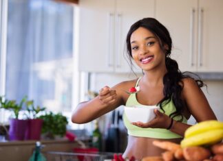 Como combinar dieta e exercício para emagrecer de forma eficaz Smiling young woman in sportswear enjoying a healthy fruit snack indoors.