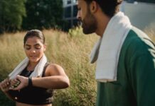 A couple outdoors using fitness trackers after a workout, wearing towels.
