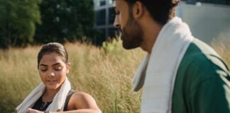 A couple outdoors using fitness trackers after a workout, wearing towels.