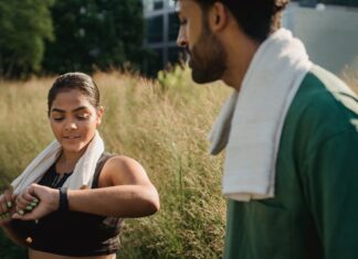 Como emagrecer correndo todos os dias: Dicas que funcionam A couple outdoors using fitness trackers after a workout, wearing towels.