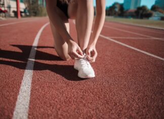 Como escolher o melhor calçado desportivo para o seu treino Close-up of a woman tying her shoes on a running track, ready to sprint.