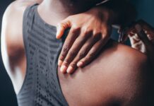 Close-up of a person holding their shoulder, wearing a black sports bra.