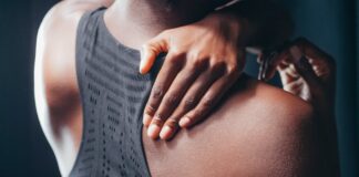 Close-up of a person holding their shoulder, wearing a black sports bra.