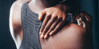 Close-up of a person holding their shoulder, wearing a black sports bra.
