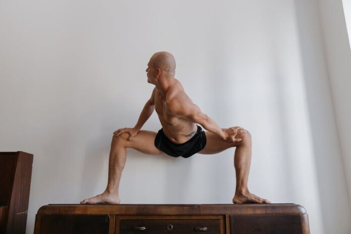 Bald man in athletic wear performing a yoga pose indoors, highlighting strength and flexibility.