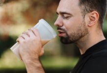 Bearded man drinking a protein shake outdoors on a sunny day, showcasing healthy living.