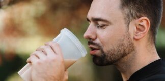Bearded man drinking a protein shake outdoors on a sunny day, showcasing healthy living.