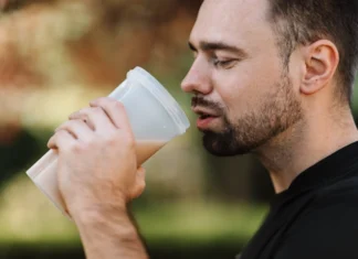 Bearded man drinking a protein shake outdoors on a sunny day, showcasing healthy living.