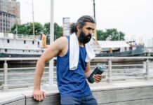 A man with a towel and water bottle rests by the waterfront after exercise.