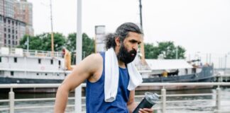 A man with a towel and water bottle rests by the waterfront after exercise.