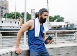 A man with a towel and water bottle rests by the waterfront after exercise.