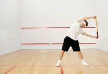 Young man stretching with a racket on an indoor squash court, preparing for a workout.