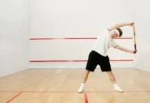 Young man stretching with a racket on an indoor squash court, preparing for a workout.