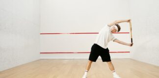 Young man stretching with a racket on an indoor squash court, preparing for a workout.