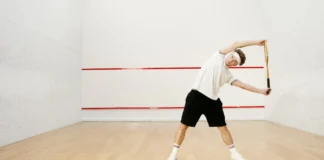 Young man stretching with a racket on an indoor squash court, preparing for a workout.