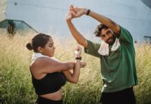 A couple engaging in outdoor stretching exercises surrounded by tall grasses on a sunny day.