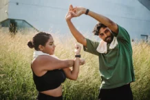 A couple engaging in outdoor stretching exercises surrounded by tall grasses on a sunny day.