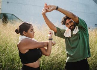 A couple engaging in outdoor stretching exercises surrounded by tall grasses on a sunny day.