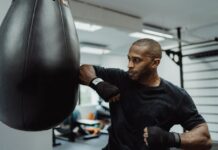 A focused boxer practices punches with a punching bag in a gym setting.