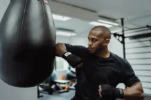 A focused boxer practices punches with a punching bag in a gym setting.