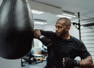 A focused boxer practices punches with a punching bag in a gym setting.
