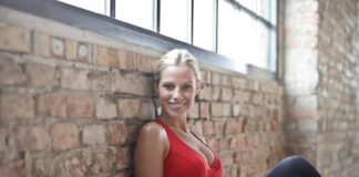 A fit woman in a red sports bra smiling while sitting against a brick wall after a workout.