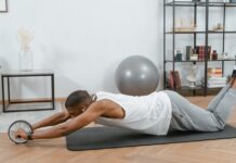 Man using an ab roller on a yoga mat indoors, promoting fitness and healthy lifestyle.
