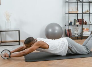 Man using an ab roller on a yoga mat indoors, promoting fitness and healthy lifestyle.