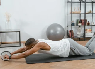 Man using an ab roller on a yoga mat indoors, promoting fitness and healthy lifestyle.