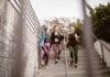 Emagrecer de forma saudável: Caminhada diária pode transformar vidas Three women walking down steps outdoors, carrying yoga mats, enjoying a fitness conversation.