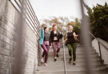 Three women walking down steps outdoors, carrying yoga mats, enjoying a fitness conversation.