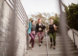 Emagrecer de forma saudável: Caminhada diária pode transformar vidas Three women walking down steps outdoors, carrying yoga mats, enjoying a fitness conversation.