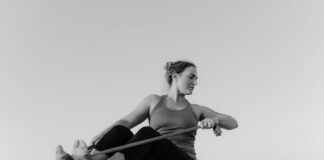 A woman practicing yoga with a resistance band on a beach in black and white.