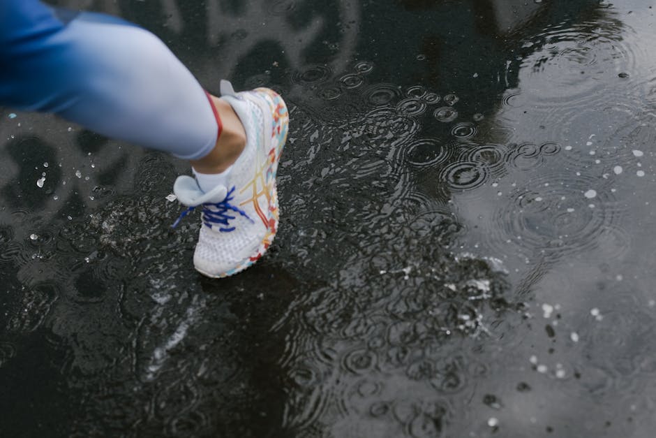 Close-up of a runner's shoe splashing through a puddle on a rainy day.