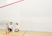 Two young squash players resting on a court, holding rackets and chatting.
